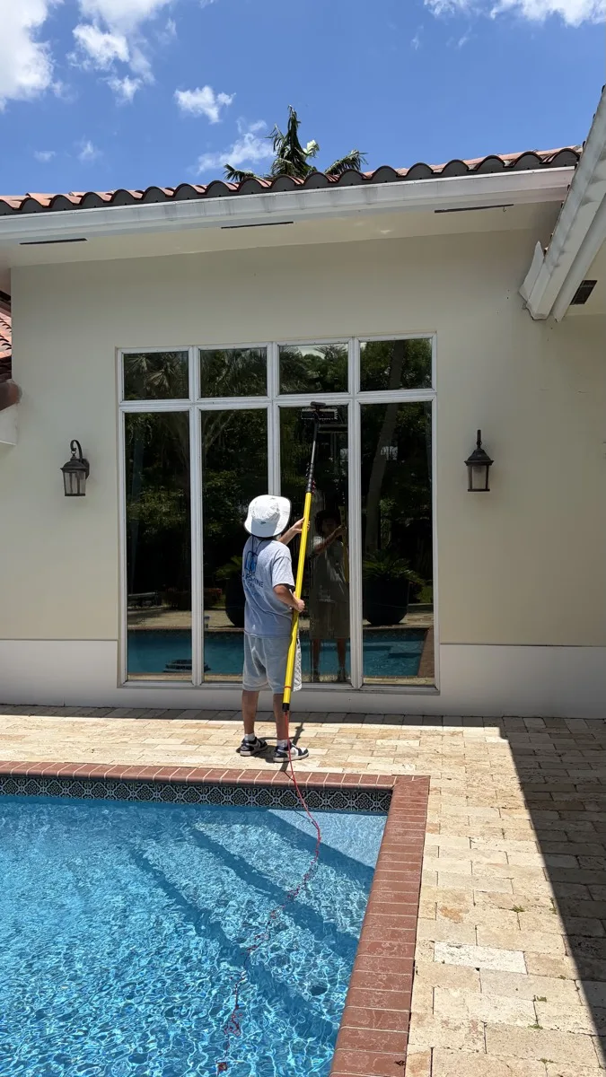 A Gulfshine technician cleaning windows beside a South Florida pool