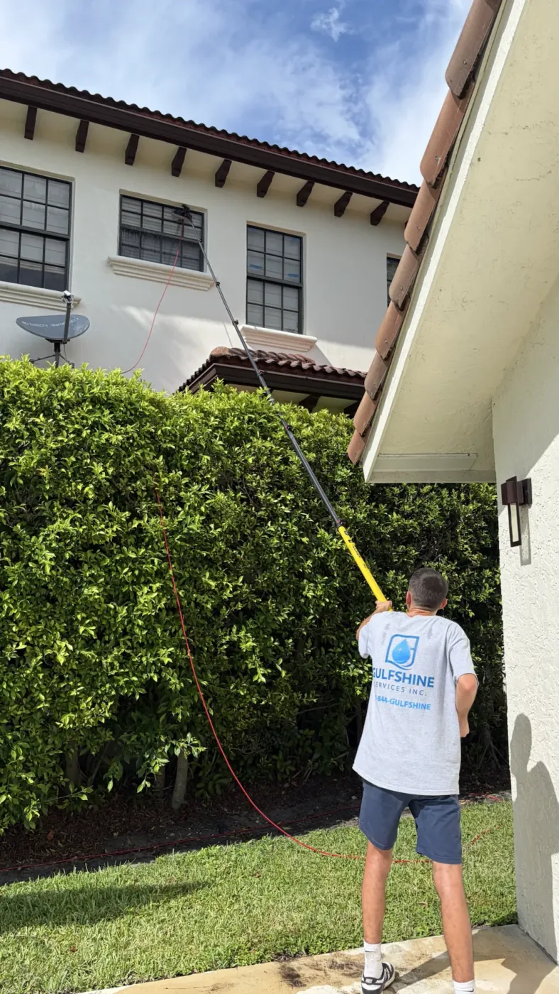 Gulfshine technician cleaning second-story windows with a water-fed pole at a South Florida home